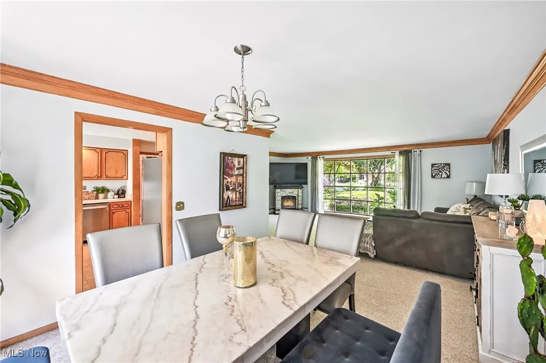 Dining room featuring crown molding, light carpet, a chandelier, and a stone fireplace