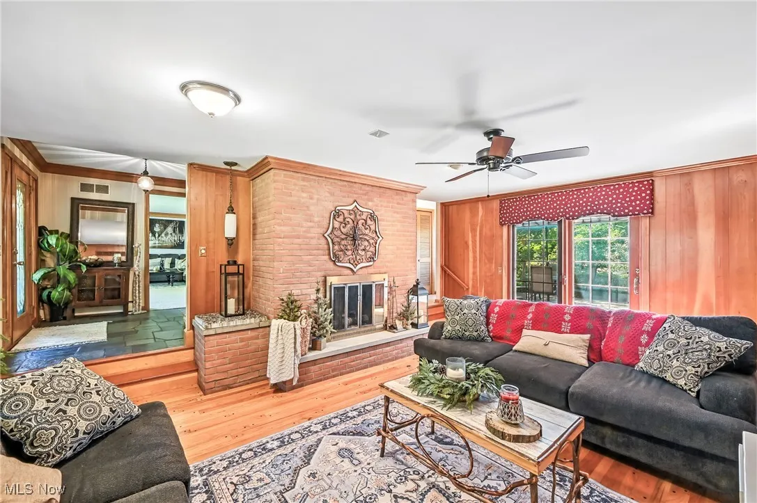 Living area featuring wood finished floors, a brick fireplace, wooden walls, and ornamental molding