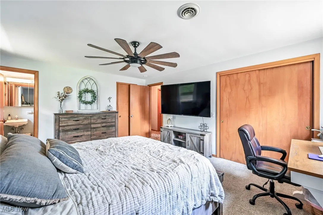 Bedroom with carpet, ceiling fan, ensuite bath, and multiple closets