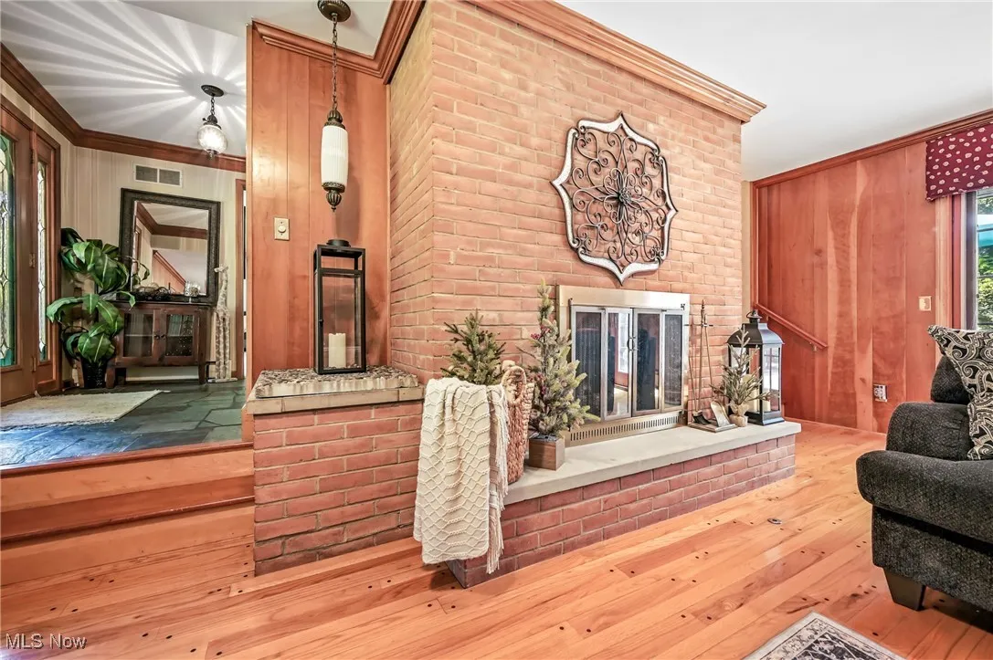 Living room with wooden walls, hardwood floors, a gas fireplace, and crown molding