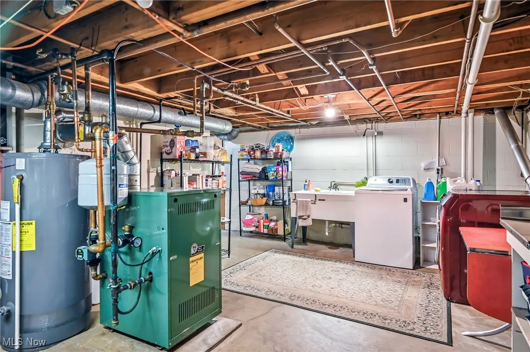 Unfinished below grade area with gas water heater, a heating unit, and washer and dryer