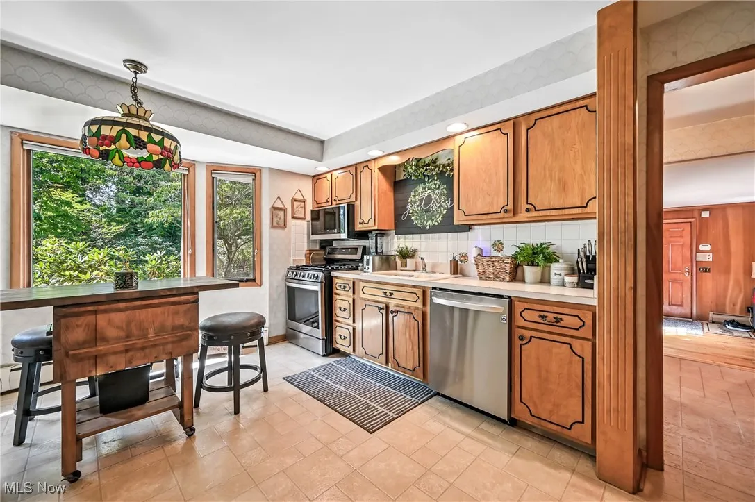 Kitchen featuring decorative light fixtures, appliances with stainless steel finishes, light countertops, tasteful backsplash, and brown cabinets