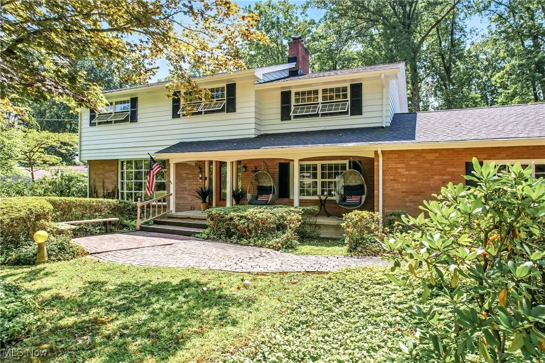 Traditional-style house with brick siding, covered porch, a chimney, a front lawn, and roof with shingles