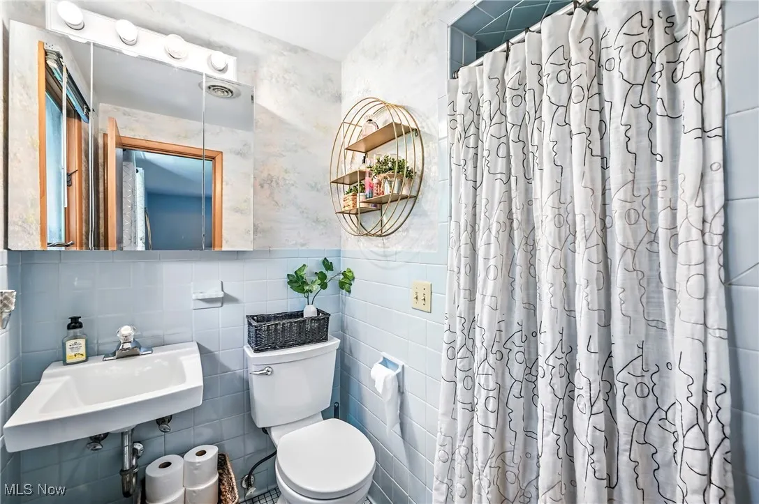 Bathroom with wallpapered walls, tile walls, curtained shower, and a wainscoted​​‌​​​​‌​​‌‌​‌‌​​​‌‌​‌​‌​‌​​​‌​​ wall