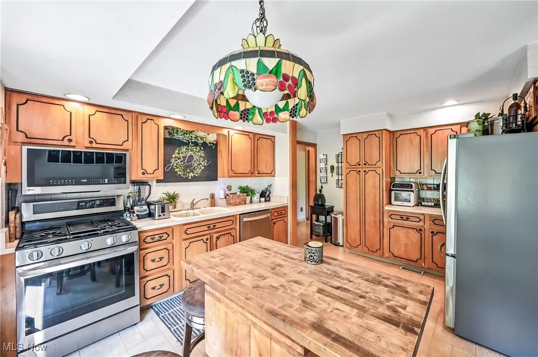 Kitchen with appliances with stainless steel finishes, light tile patterned flooring, light countertops, brown cabinetry, and recessed lighting