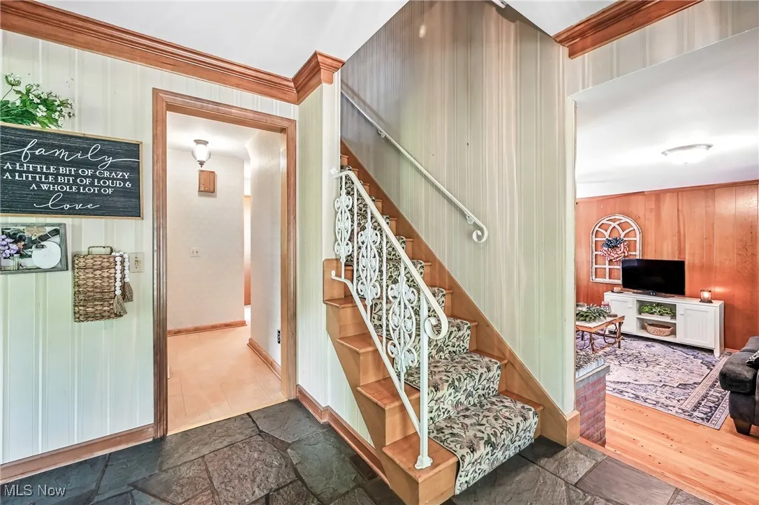 Stairs with wooden walls, ornamental molding, and stone tile flooring