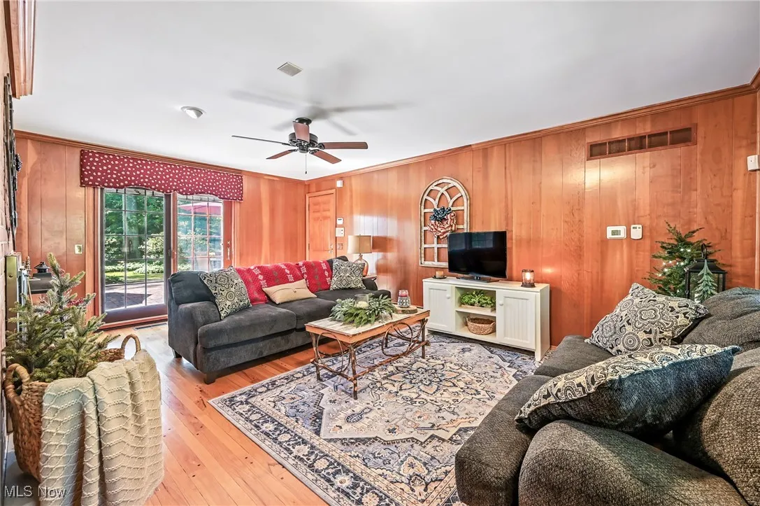 Living area with wood walls, ornamental molding, hardwood floors, and a ceiling fan