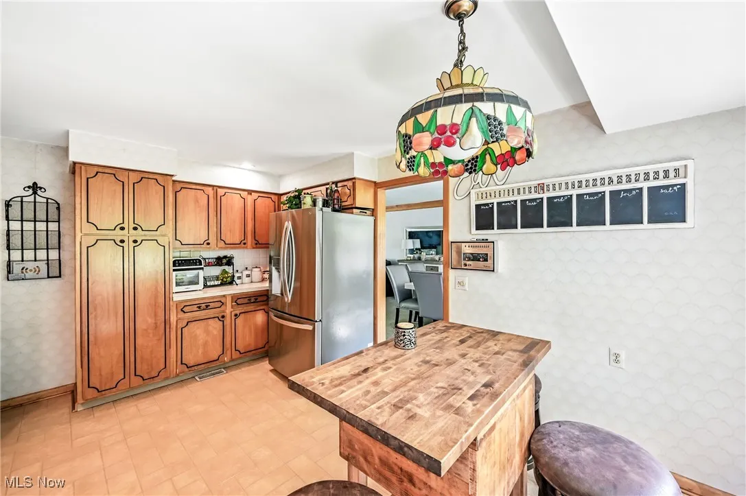 Kitchen featuring wallpapered walls, stainless steel fridge with ice dispenser, brown cabinets, light countertops.