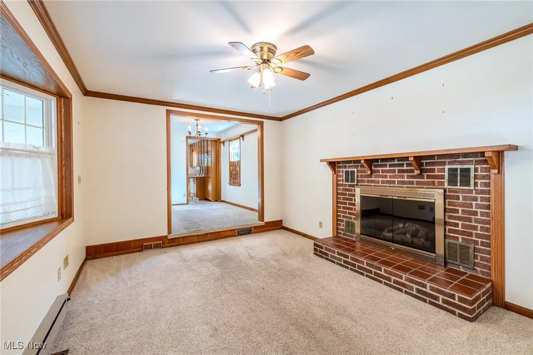 Unfurnished Family room with carpet floors, ornamental molding, a fireplace, a baseboard heating unit, and a ceiling fan