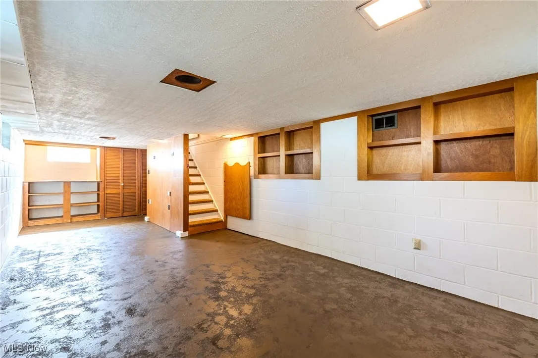 Basement featuring concrete block wall, a textured ceiling, and stairs