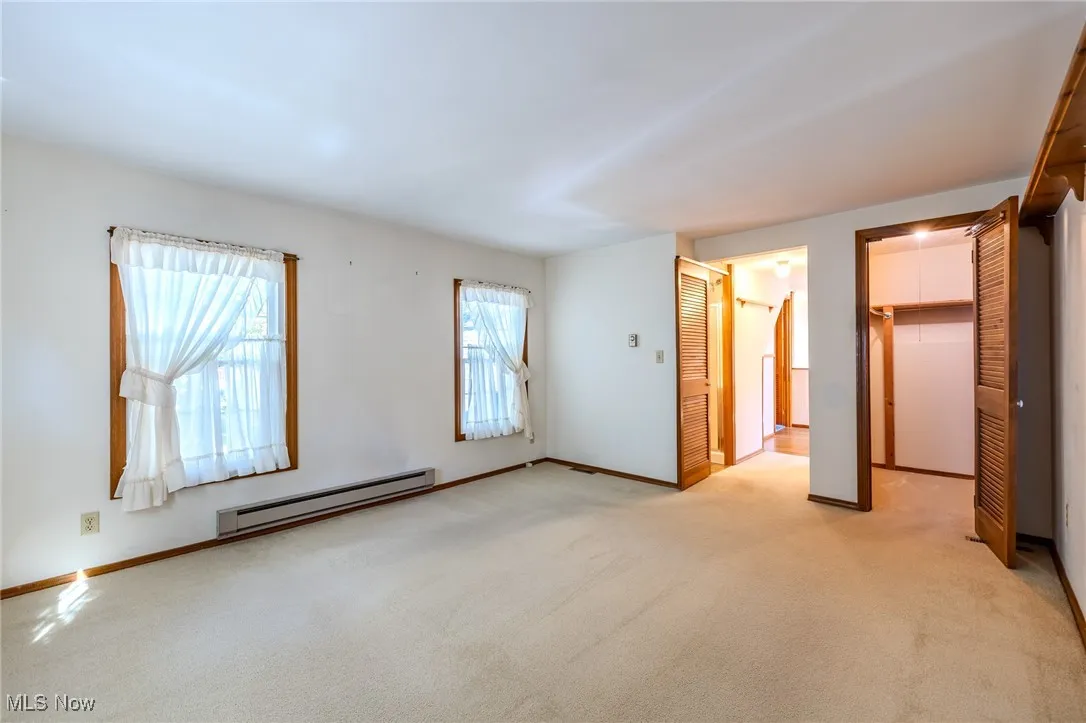 Unfurnished bedroom with a baseboard heating unit, light colored carpet, and a spacious closet