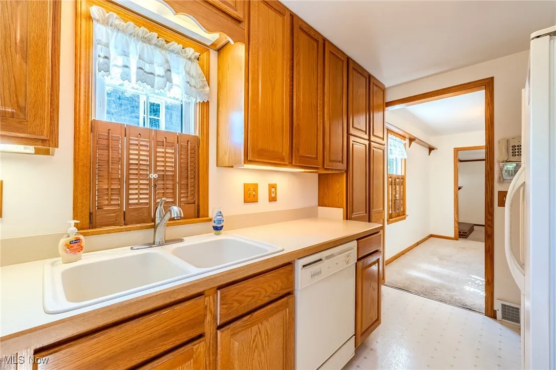 Kitchen featuring light countertops, white appliances, light flooring, and brown cabinets