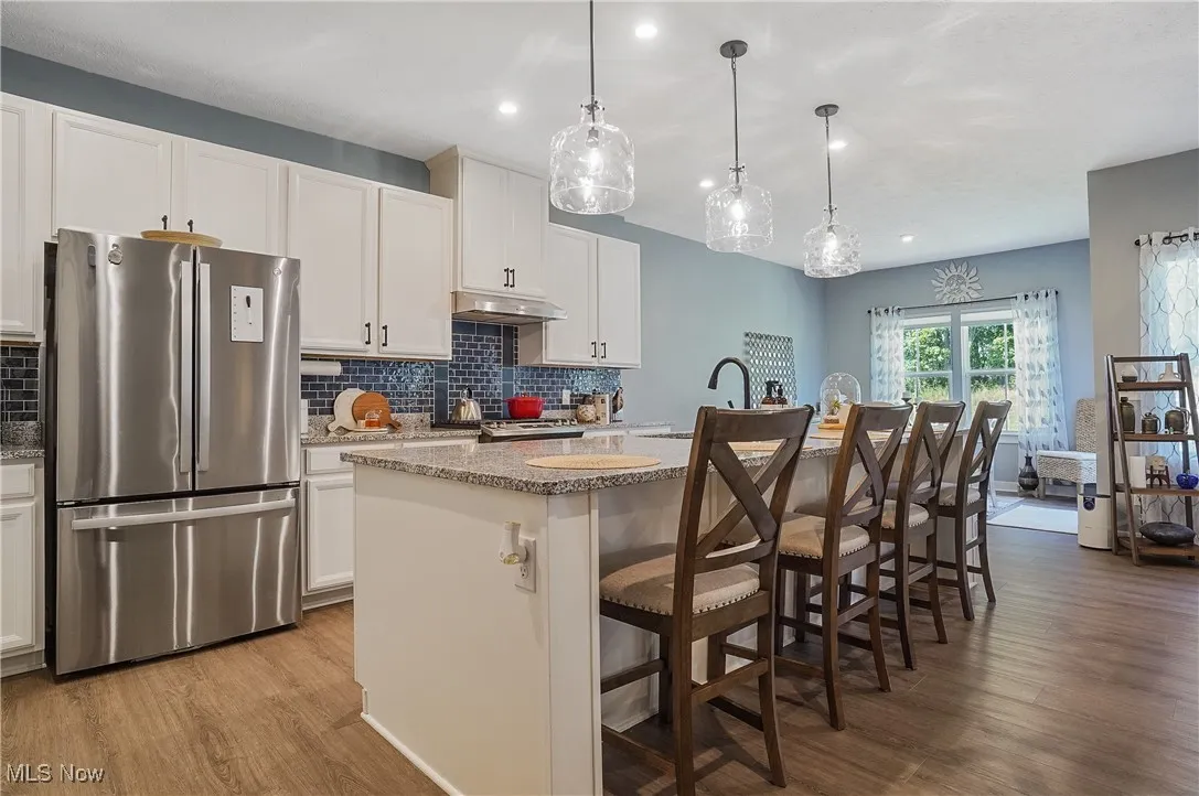 Kitchen featuring freestanding refrigerator, a breakfast bar, a center island with sink, light stone counters, and light wood-type flooring