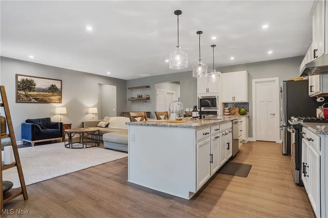 Kitchen with white cabinets, light stone countertops, recessed lighting, stainless steel appliances, and light wood-style floors