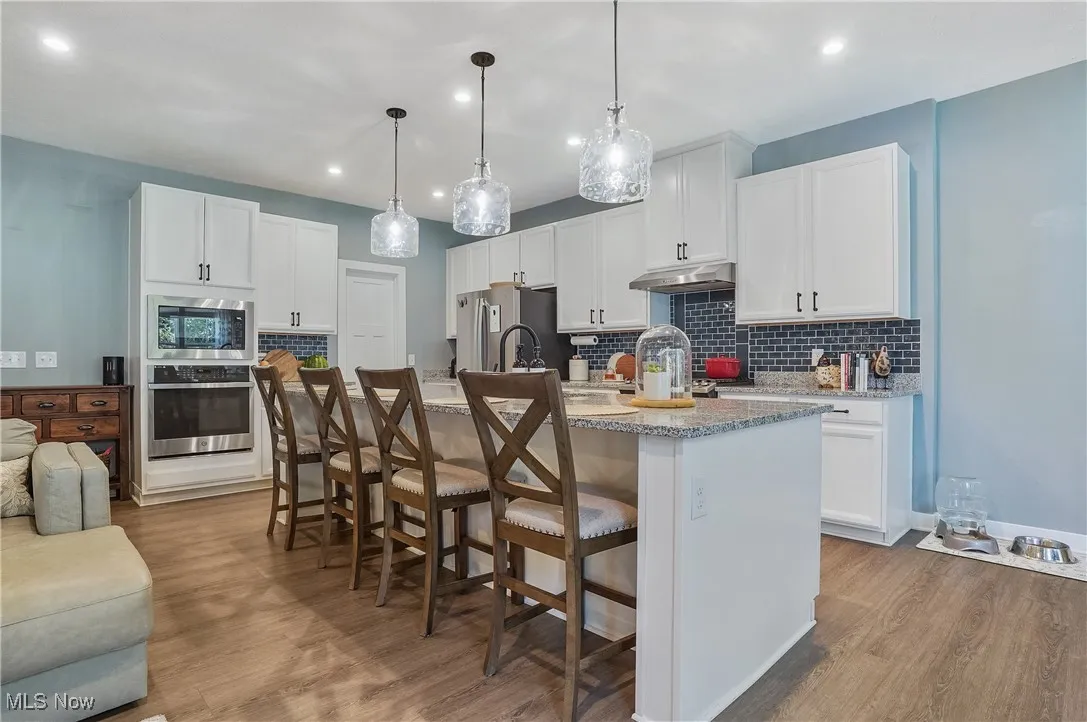 Kitchen featuring a breakfast bar, tasteful backsplash, appliances with stainless steel finishes, an island with sink, and white cabinetry