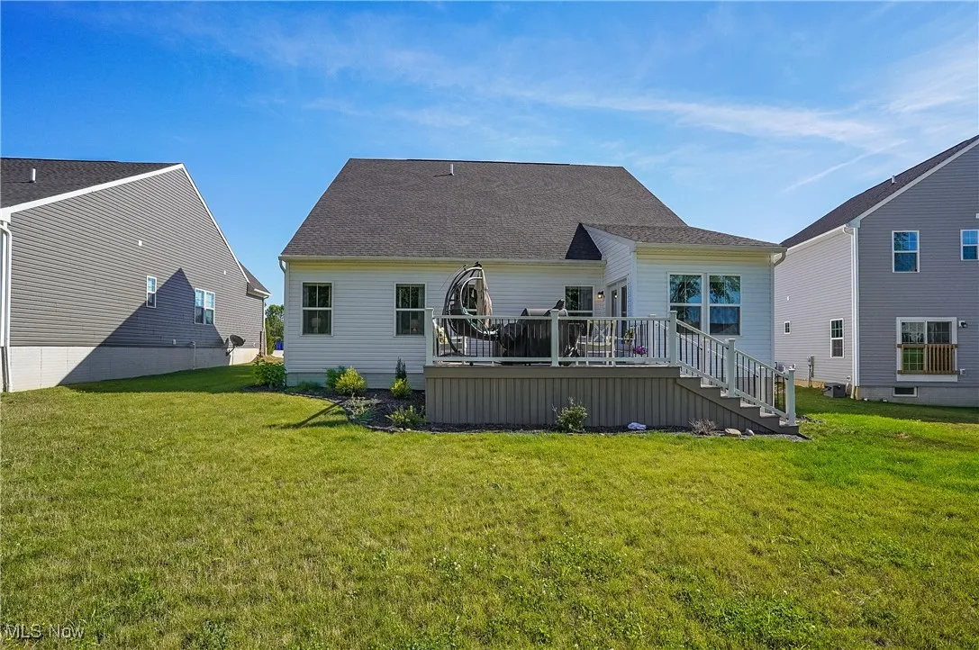 Rear view of property featuring a deck, a lawn, stairway, and roof with shingles