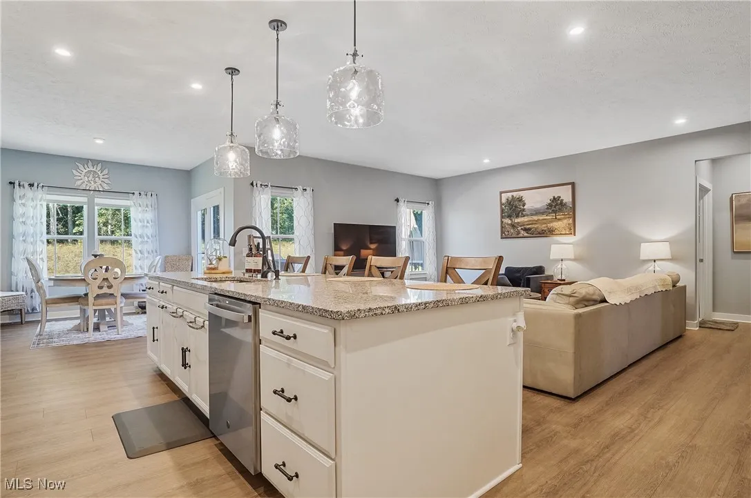 Kitchen with open floor plan, light stone counters, white cabinets, recessed lighting, and a kitchen island with sink