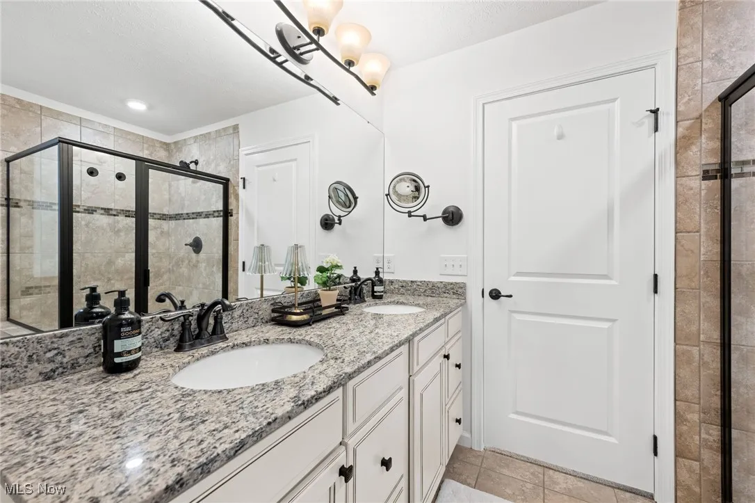 Owner's bath featuring a shower stall, double vanity, and light tile patterned flooring