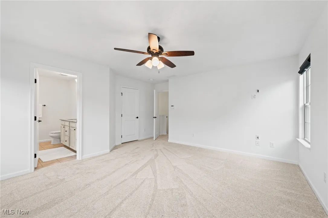 Owner's suite featuring light carpet, ceiling fan, and connected bathroom