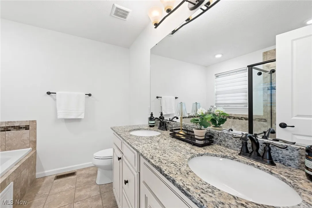 Owner's bathroom with double vanity, a tub, a stall shower, and light tile patterned flooring