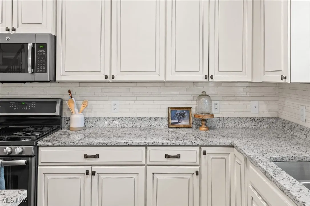 Kitchen featuring stainless steel appliances, decorative backsplash, ample cabinets, and light stone countertops