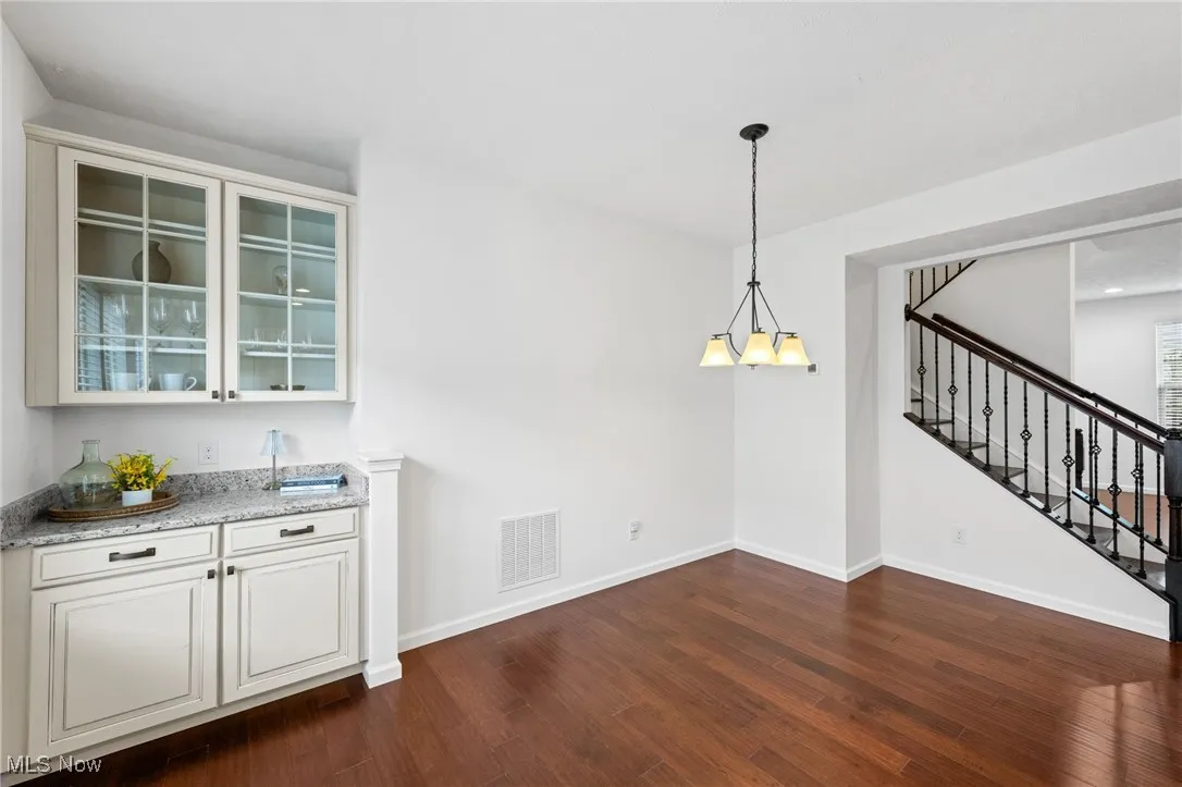 Unfurnished dining area featuring dark wood finished floors, stairway, a chandelier, and bar area
