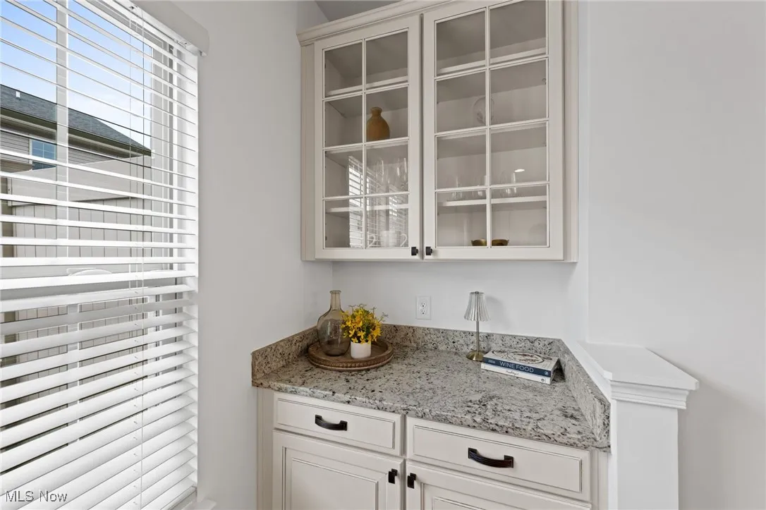 Bar area with white cabinetry, light stone countertops, and glass insert cabinets