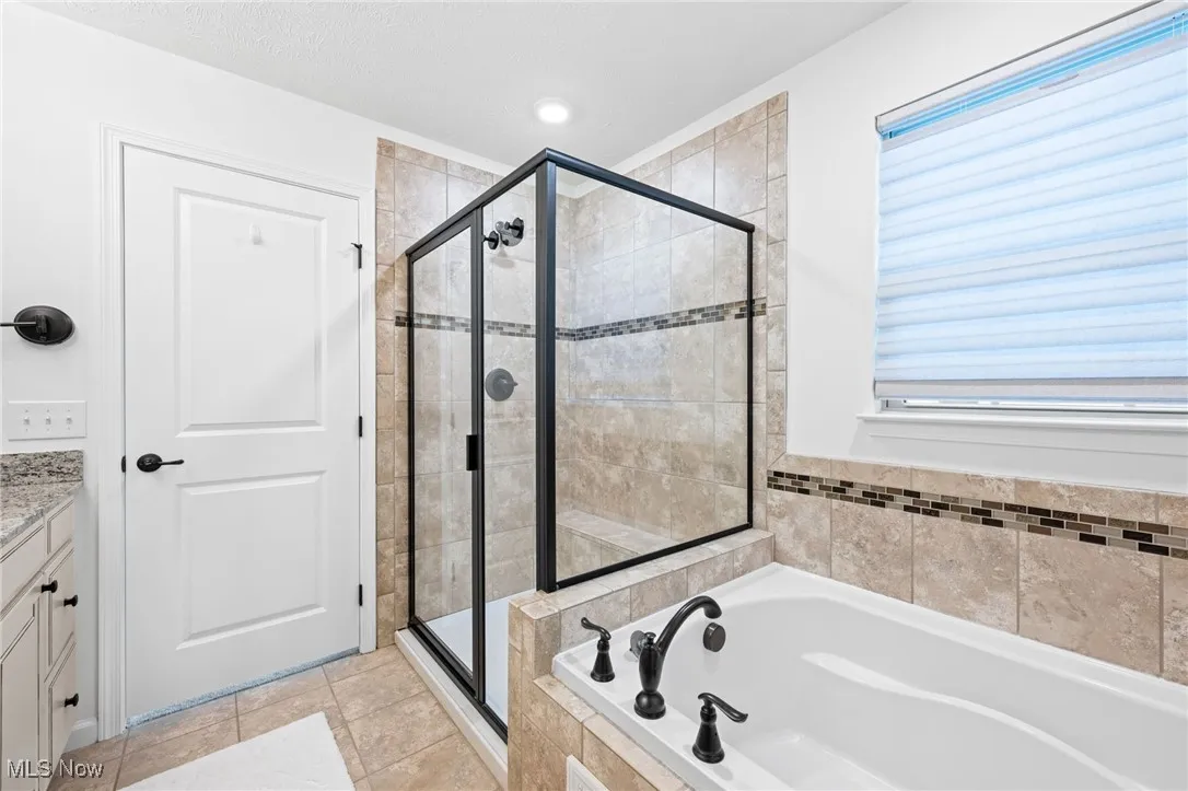 Owner's bathroom featuring a stall shower, a bath, vanity, and light tile patterned floors