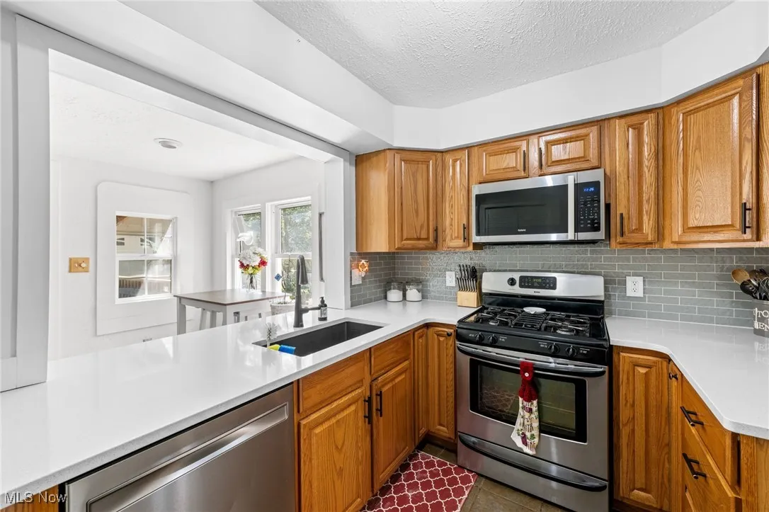 Kitchen with appliances with stainless steel finishes, brown cabinetry, a textured ceiling, light stone counters, and tasteful backsplash