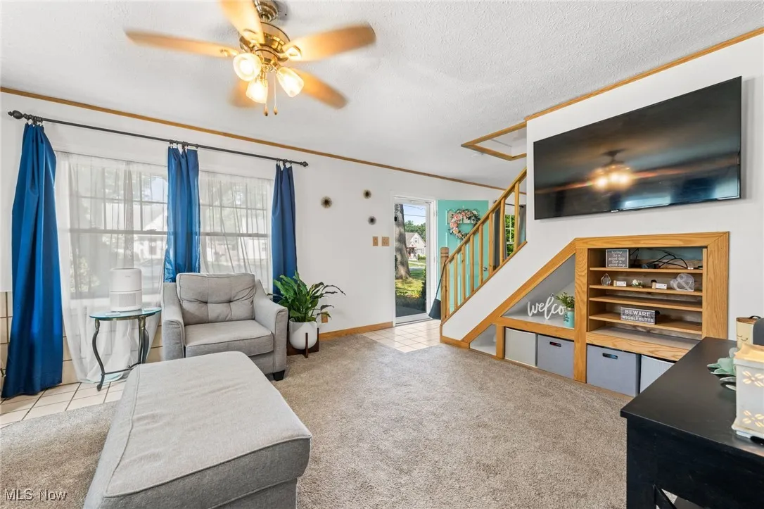 Living area featuring a ceiling fan, light carpet, a textured ceiling, crown molding, and stairway