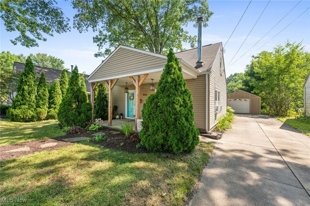 View of front of property featuring an outbuilding, a front lawn, a garage, covered porch, and a shingled roof