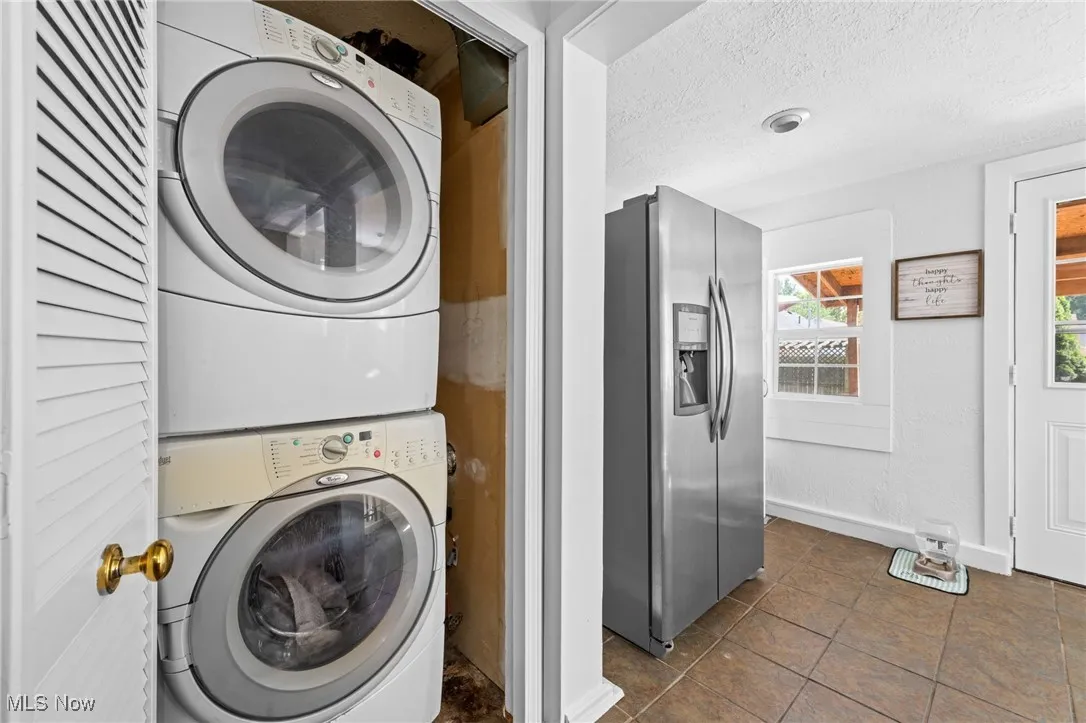 Laundry area featuring a textured ceiling, stacked washer and clothes dryer, and dark tile patterned floors