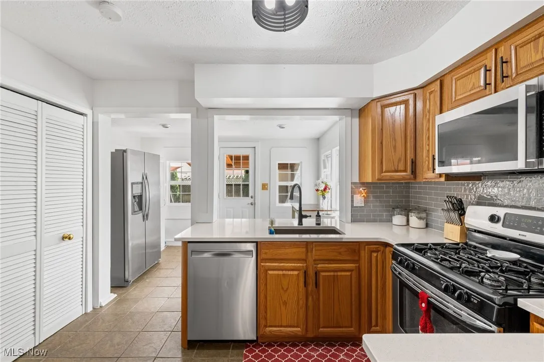 Kitchen with stainless steel appliances, brown cabinetry, decorative backsplash, a peninsula, and dark tile patterned floors