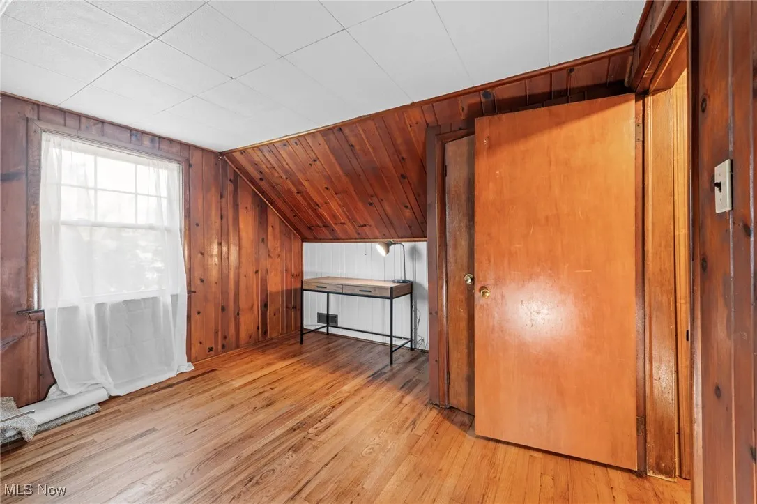Additional living space featuring wooden walls, light wood finished floors, and vaulted ceiling