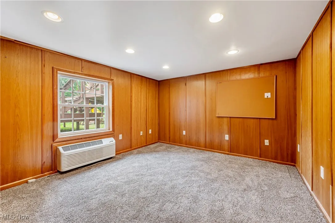 Empty room featuring recessed lighting, light carpet, wood walls, and a wall mounted air conditioner