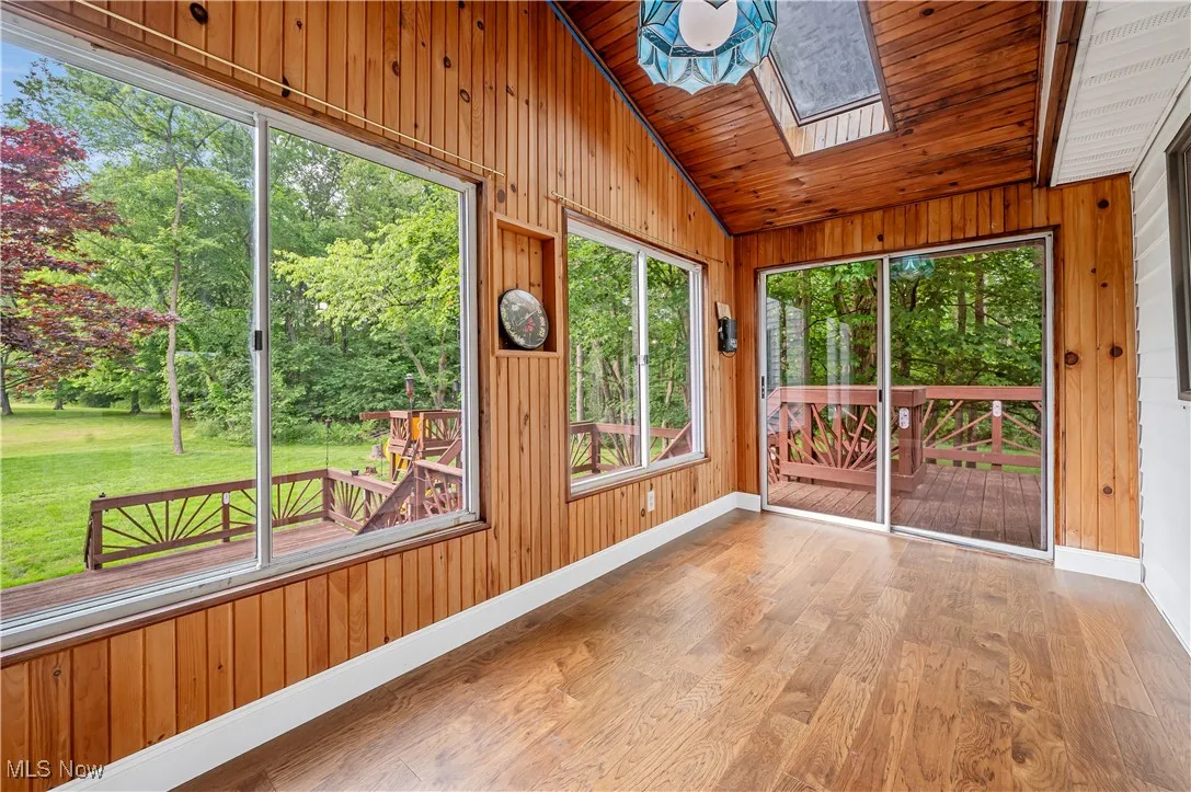 Unfurnished sunroom featuring lofted ceiling, a skylight, wood walls, wood finished floors, and wooden ceiling