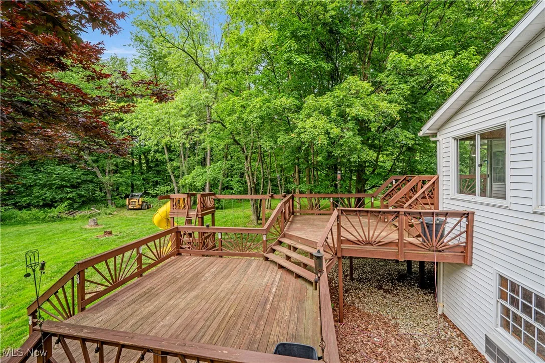 Wooden deck with a playground, a yard, and view of scattered trees
