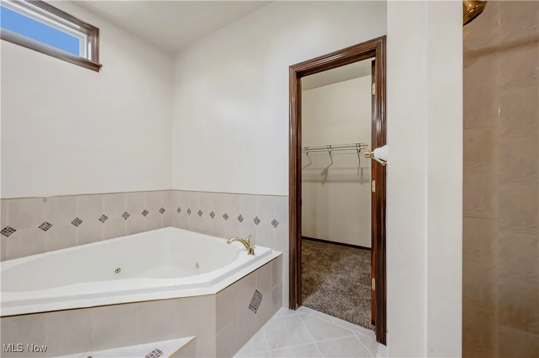 Bathroom featuring light tile patterned floors, a tub with jets, and a spacious closet