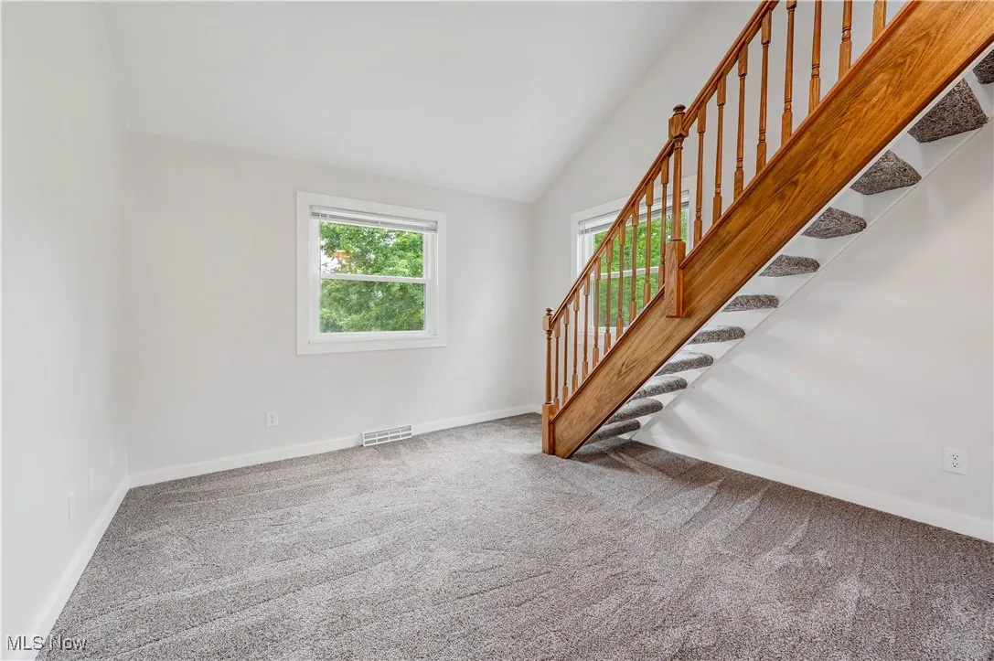 Unfurnished room featuring lofted ceiling, carpet floors, and stairs