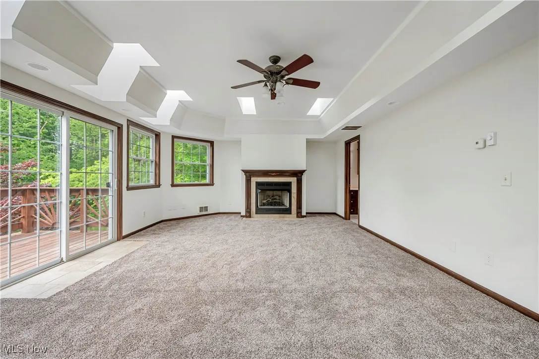 Unfurnished living room with a raised ceiling, a fireplace with flush hearth, light colored carpet, and a skylight