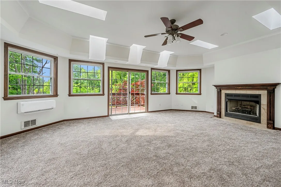 Unfurnished living room with a skylight, a raised ceiling, carpet flooring, a tile fireplace, and a ceiling fan
