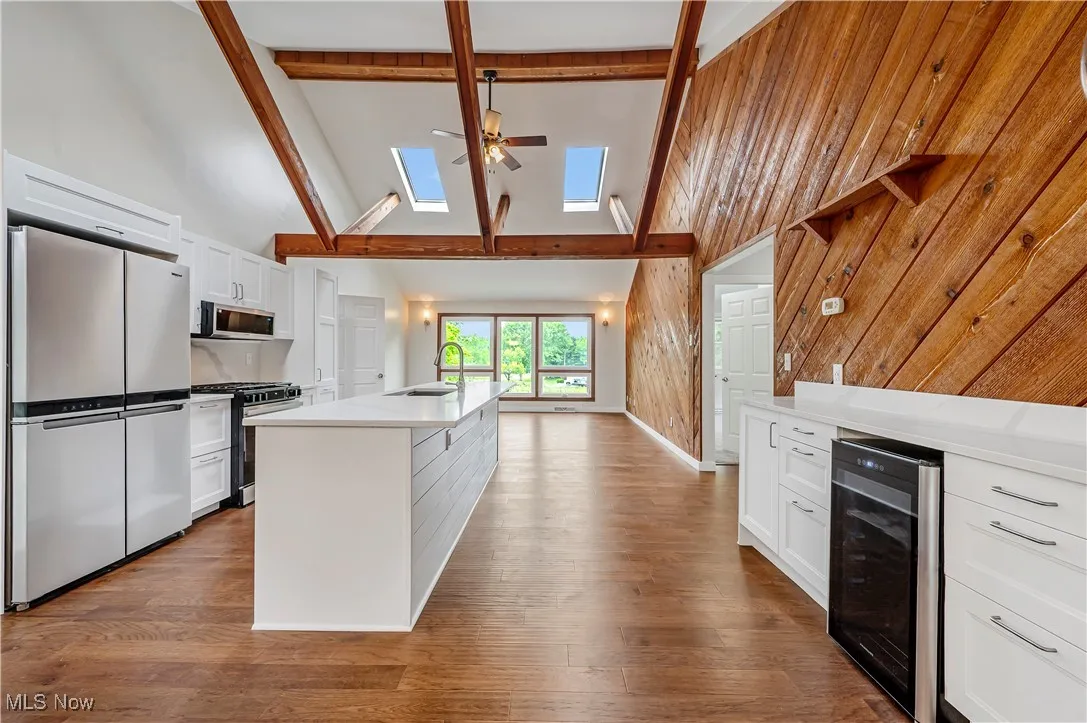 Kitchen featuring white cabinetry, high vaulted ceiling, stainless steel appliances, beam ceiling, and wine cooler