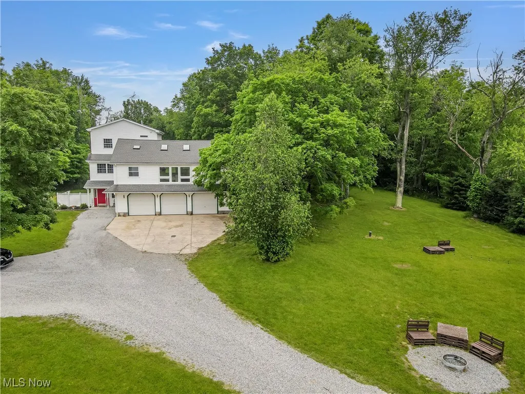 View of front of house featuring gravel driveway, an attached garage, a front lawn, a shingled roof, and an outdoor fire pit