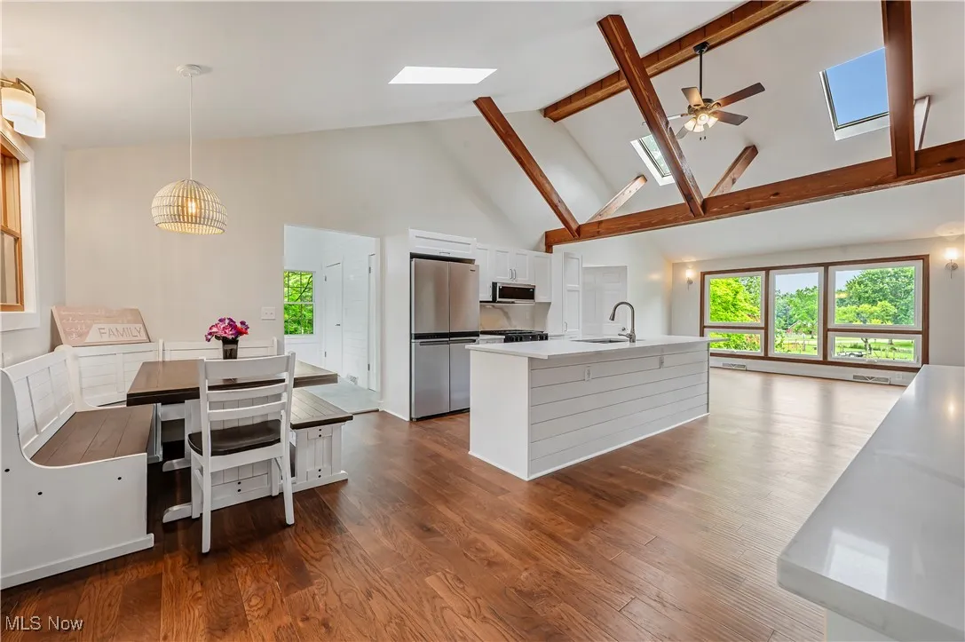 Kitchen featuring a skylight, high vaulted ceiling, white cabinets, dark wood-style flooring, and stainless steel appliances