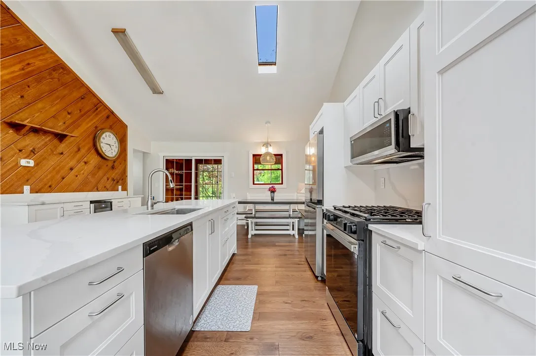 Kitchen with white cabinetry, appliances with stainless steel finishes, a skylight, light wood-style flooring, and wood walls