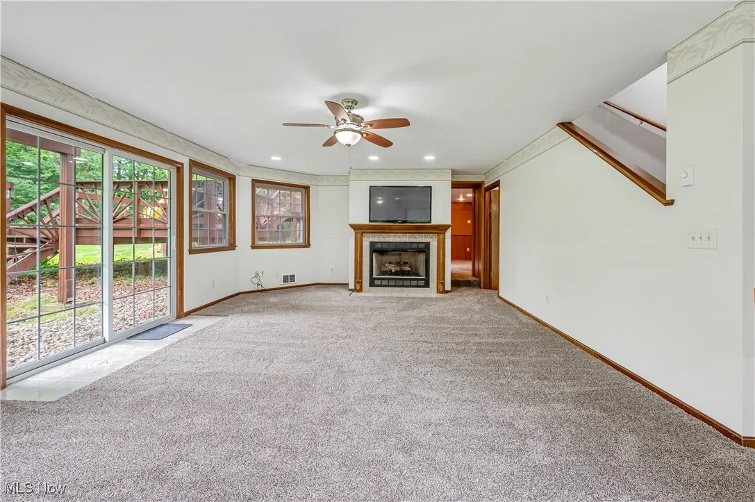 Unfurnished living room with a tiled fireplace, carpet floors, ceiling fan, and recessed lighting