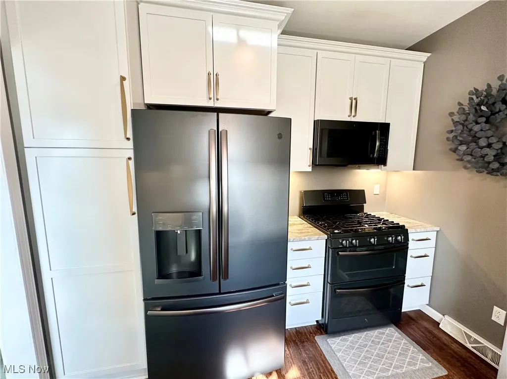 Kitchen featuring black appliances, white cabinets, and wood finished floors