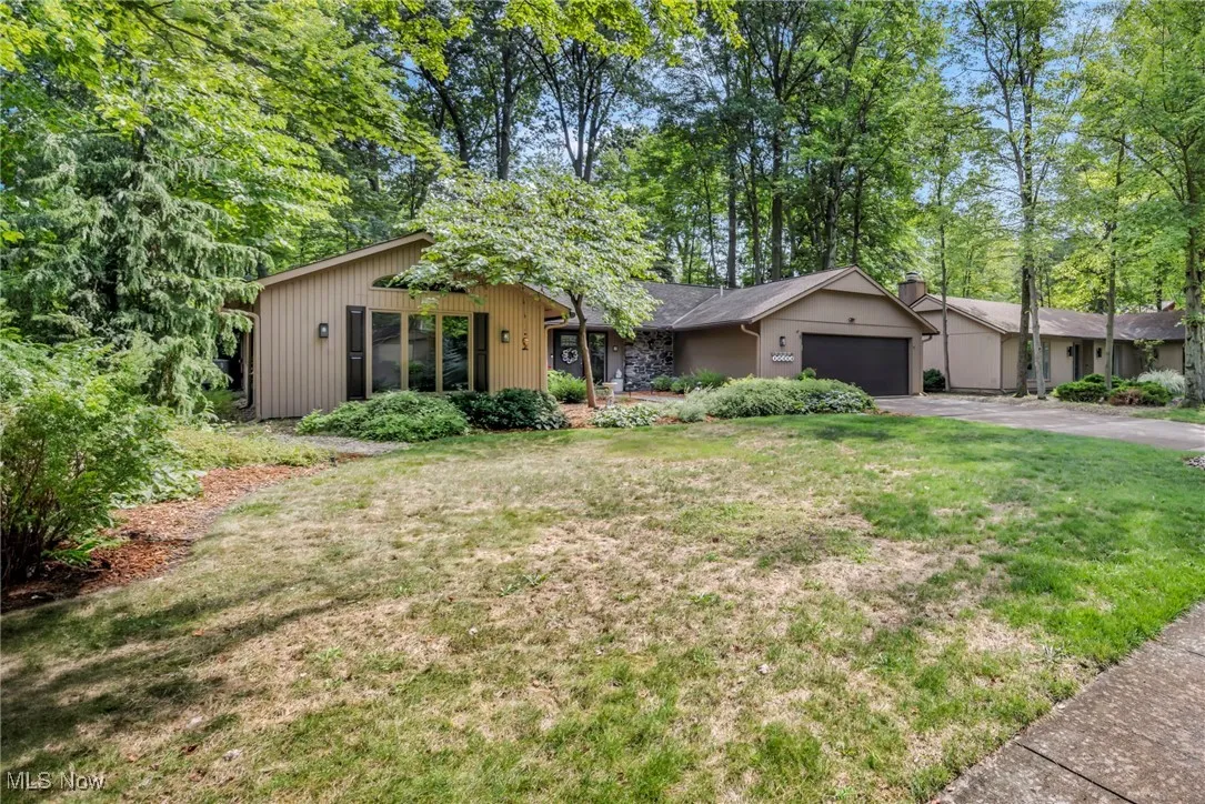 View of front of property featuring an attached garage, driveway, a front yard, and view of scattered trees