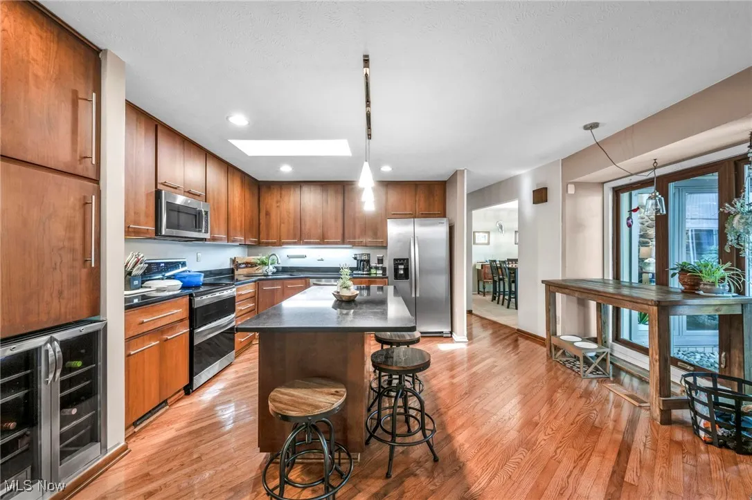 Kitchen featuring beverage cooler, a skylight, appliances with stainless steel finishes, a kitchen breakfast bar, and brown cabinets