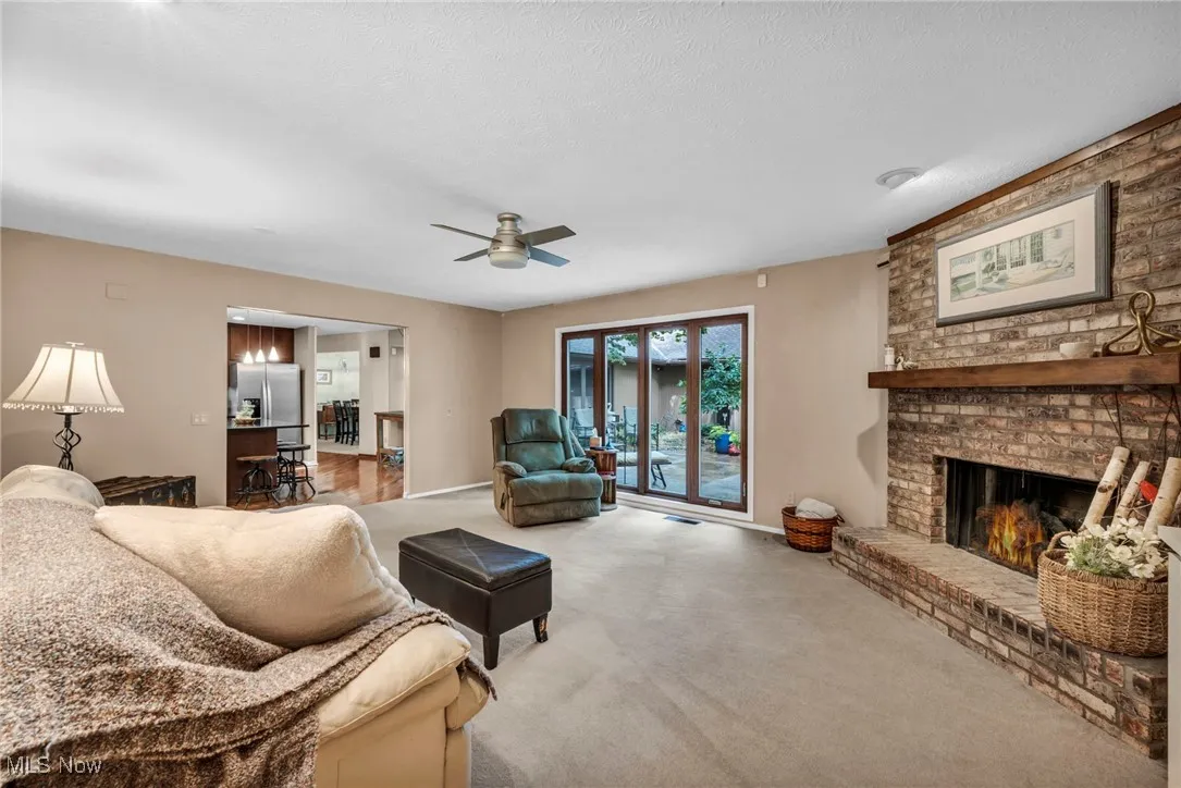 Living room featuring carpet flooring, a ceiling fan, a brick fireplace, and a textured ceiling